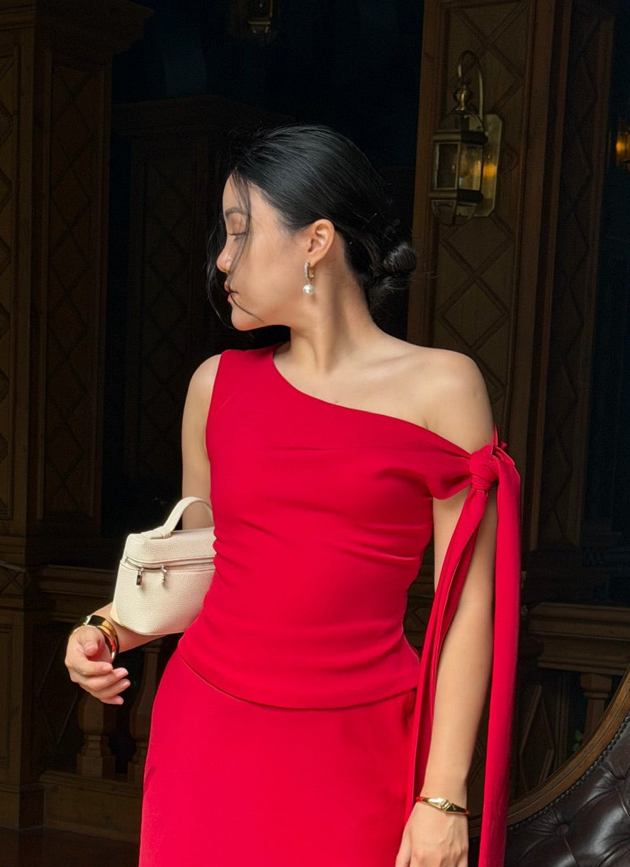 Woman in a red one-shoulder dress standing in an elegant interior setting.