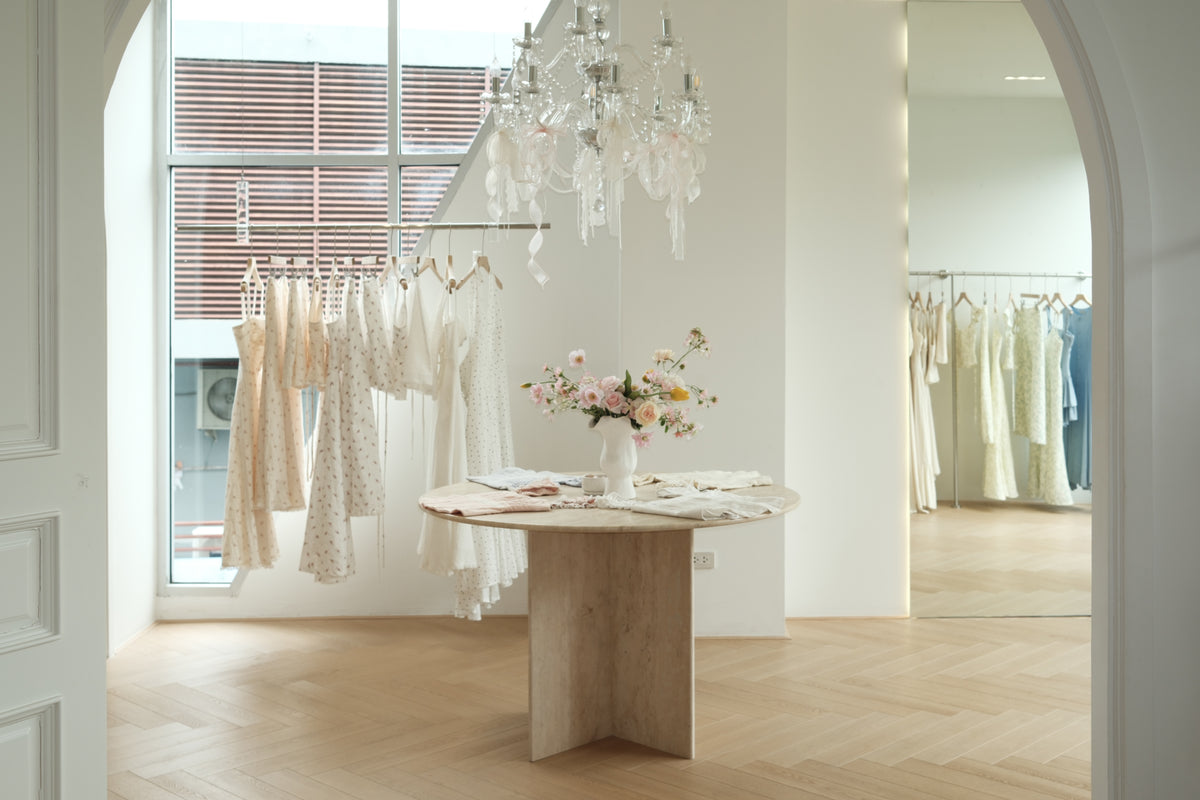 Inside the RAVii boutique in Phrom Phong, Bangkok: floral dresses on a rail, a crystal chandelier and a travertine table with pink flowers