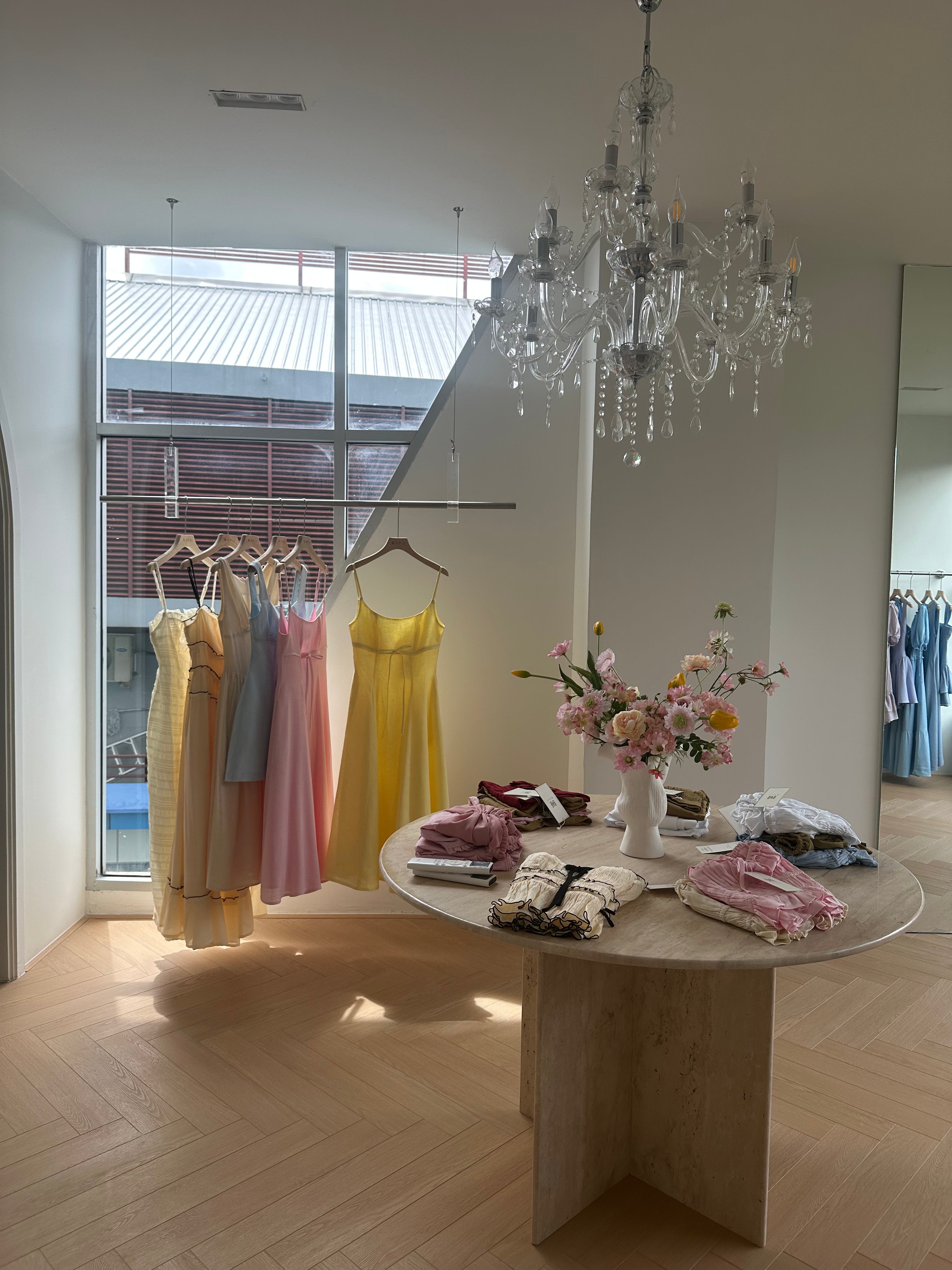 Dresses hanging on a rack with a table displaying more dresses and flowers in a stylish room.