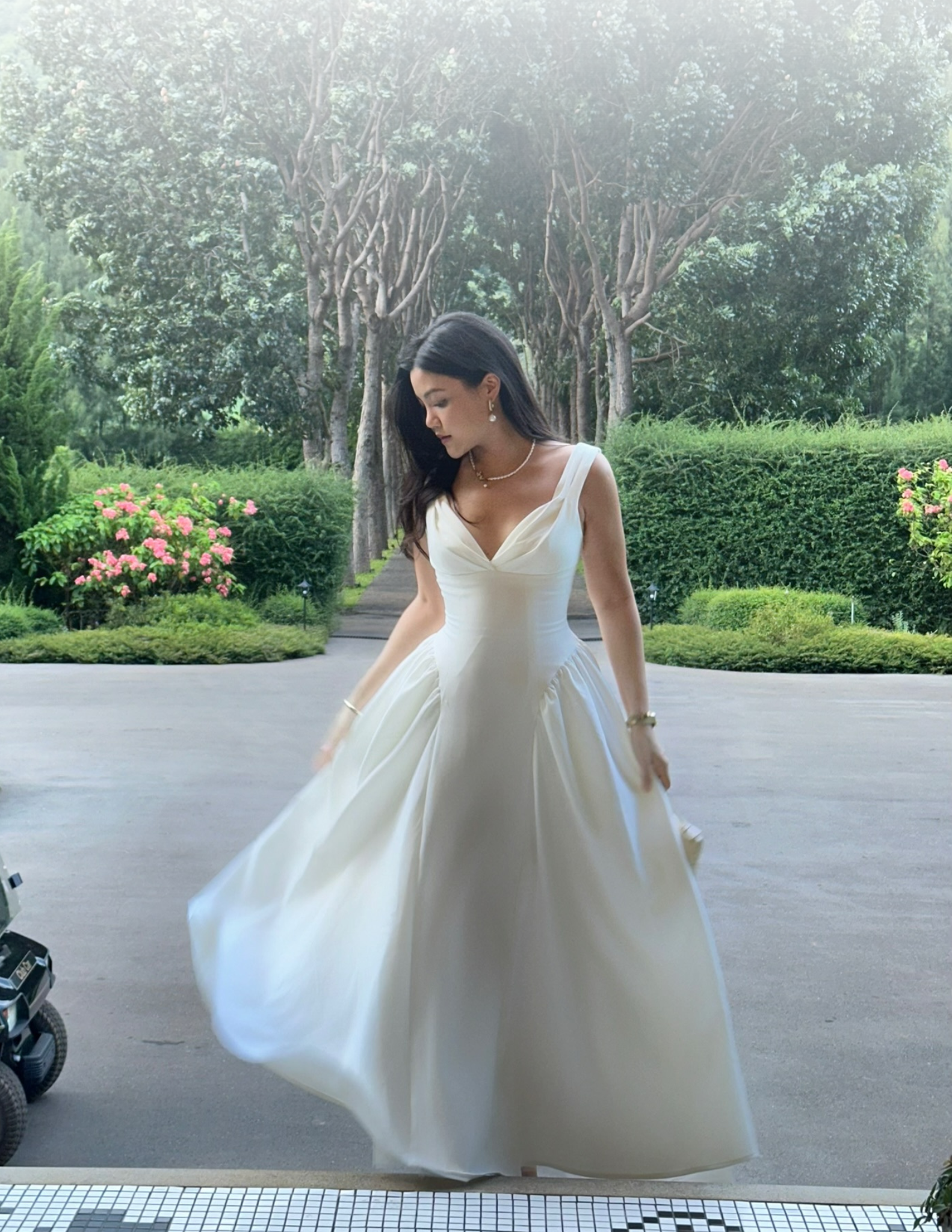Woman in a white RAVii dress standing outdoors with greenery in the background